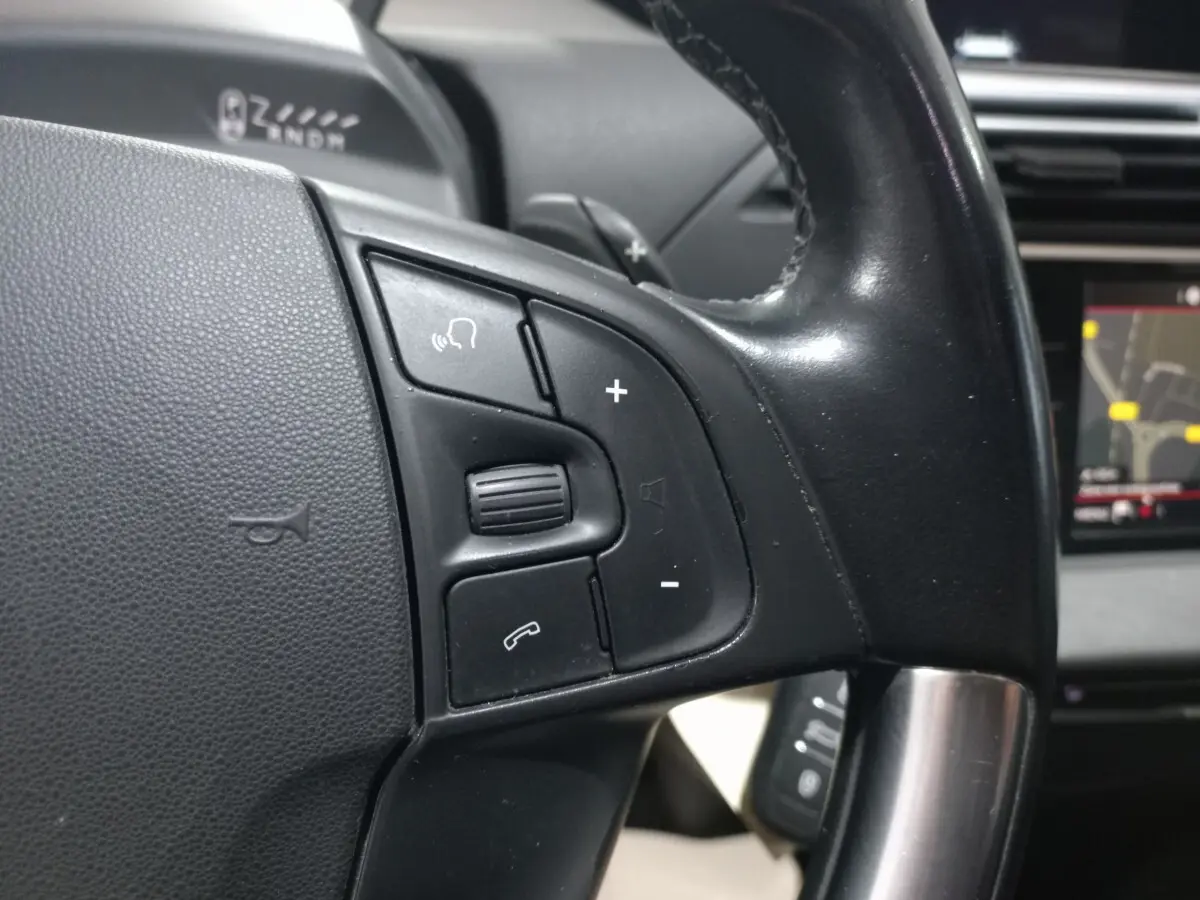 Gros plan sur les commandes gauche du volant noir du Citroën Grand C4 Spacetourer avec écran tactile de navigation visible.