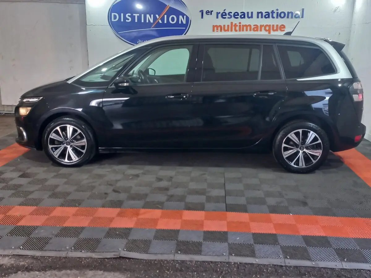 Vue de profil côté gauche d'un Citroën Grand C4 Spacetourer noir stationné en intérieur sur sol à damiers.