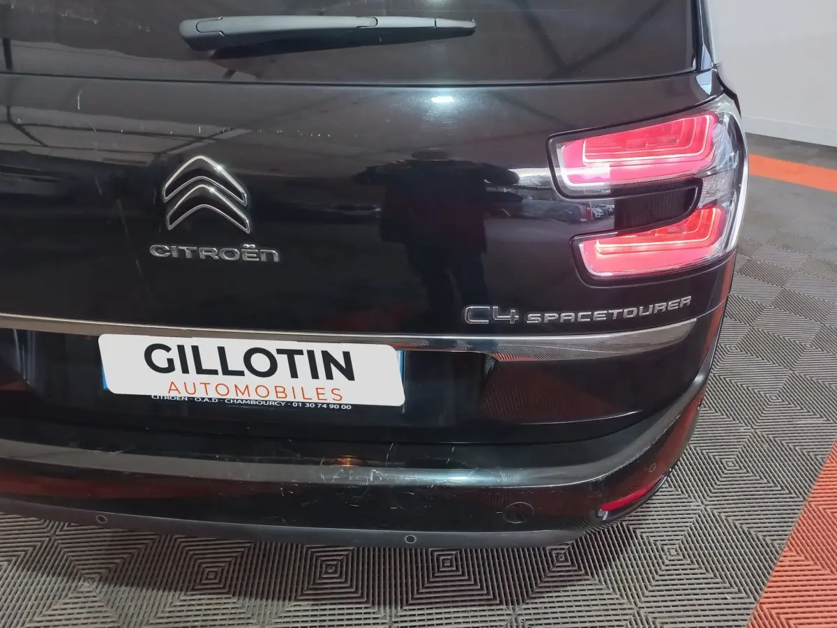 Vue arrière droite d'un Citroën Grand C4 Spacetourer noir avec feux arrière allumés et logo visible.