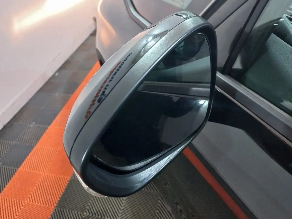 Rétroviseur extérieur droit gris métallisé du Citroën Grand C4 Spacetourer, vue rapprochée sur fond de sol noir et orange.