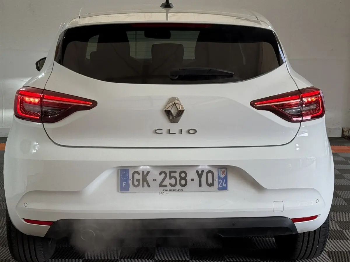 Vue arrière d'une Renault Clio blanche avec feux LED allumés et plaque d'immatriculation française visible.