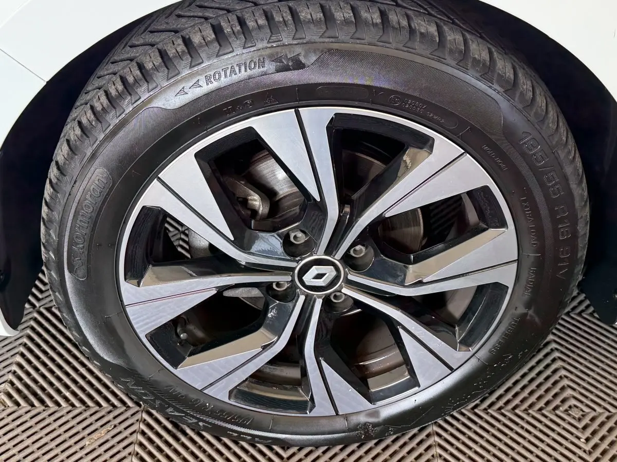 Gros plan sur la jante alliage bicolore et pneu d’une Renault Clio blanche, partie avant gauche visible.