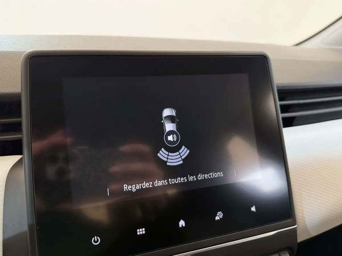 Écran tactile central de la Renault Clio Business blanc, affichant l'alerte de détection d'obstacles au stationnement.