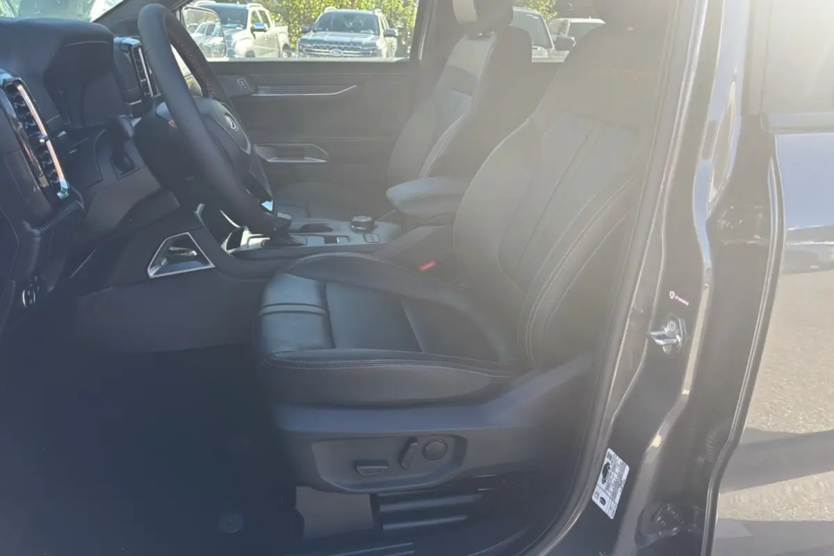 Vue intérieure côté conducteur du Ford Ranger gris carbone 2025, sièges cuir Wildtrak avec surpiqûres orange.