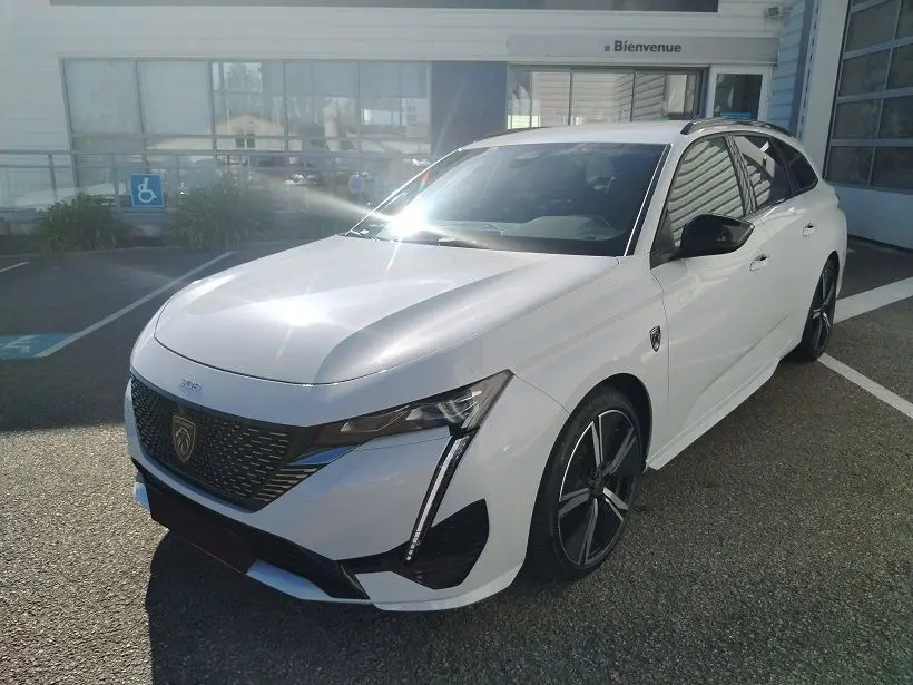 Peugeot 308 SW Hybrid 145 GT blanc Okenite vue 3/4 avant droit, avec calandre noire et jantes alliage noires.