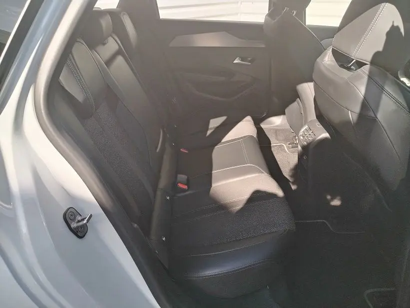 Vue intérieure arrière côté gauche du Peugeot 308 SW Hybrid 145 GT blanc Okenite, sièges en tissu noir avec surpiqûres.