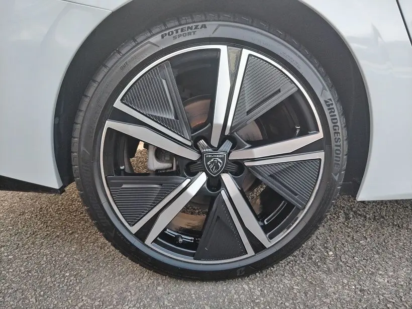 Gros plan sur la roue avant droite d’une Peugeot 308 SW Hybrid 145 GT blanche, avec jante noire et argentée au design moderne.