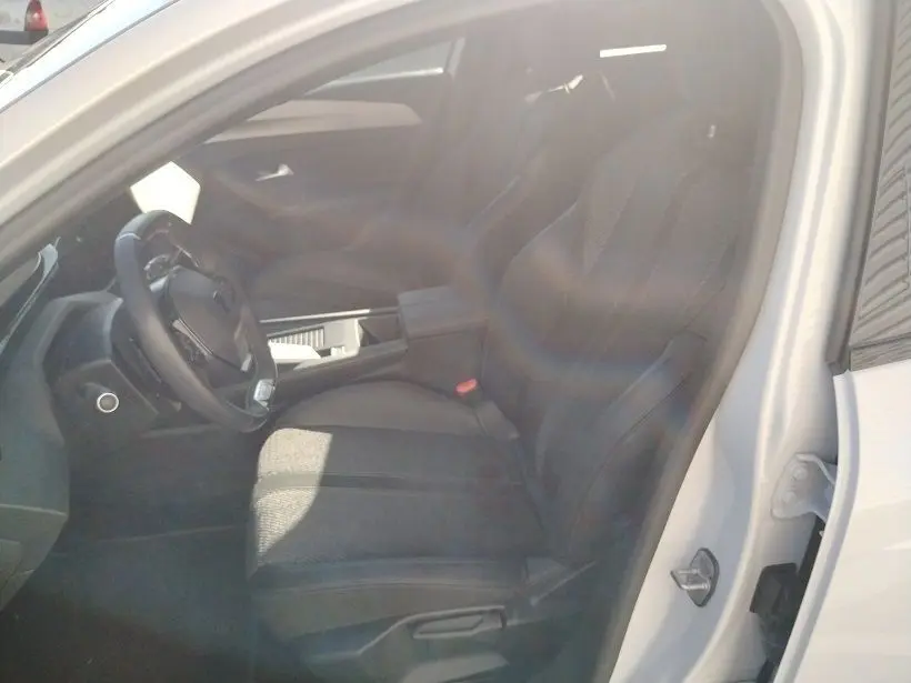 Vue intérieure côté conducteur du Peugeot 308 SW Hybrid 145 GT blanc Okenite, montrant le siège et le volant.
