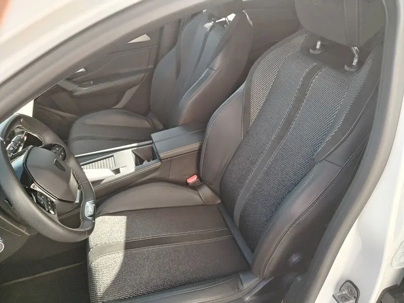Vue intérieure côté conducteur de la Peugeot 308 SW Hybrid 145 GT, sièges noirs en tissu et cuir, volant multifonction.