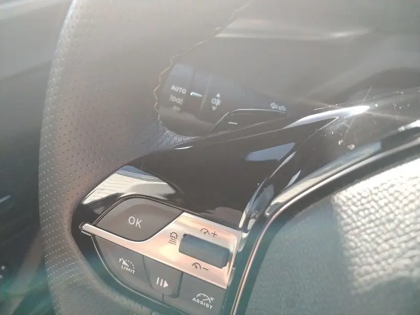 Gros plan sur les commandes au volant en cuir perforé du Peugeot 308 SW Hybrid 145 GT, finition noire brillante.