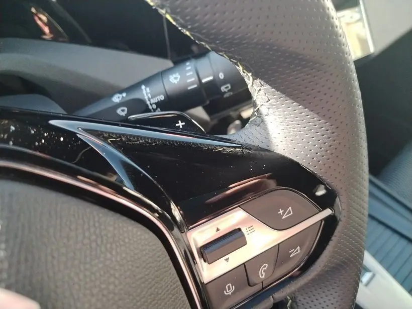 Gros plan sur les commandes au volant en cuir perforé noir et gris du Peugeot 308 SW Hybrid 145 GT, avec touches de réglage audio.