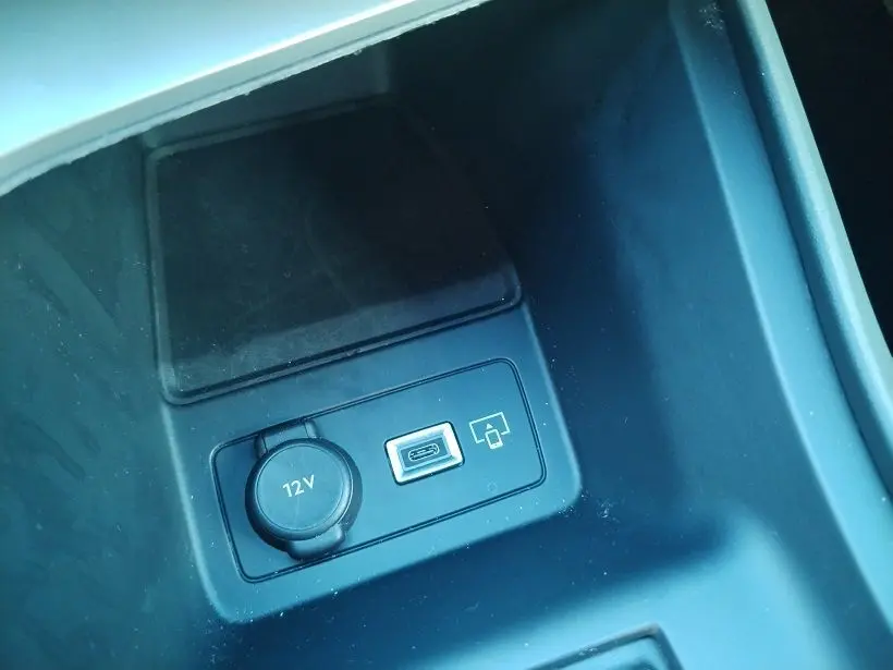 Gros plan sur la console centrale noire du Peugeot 308 SW Hybrid 2025, montrant prise 12V et port USB.