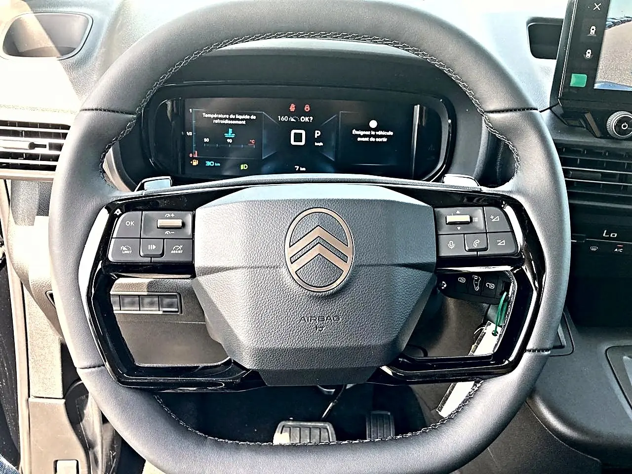 Vue rapprochée du volant cuir noir multifonction du Citroën Berlingo 2026 avec tableau de bord numérique en arrière-plan.