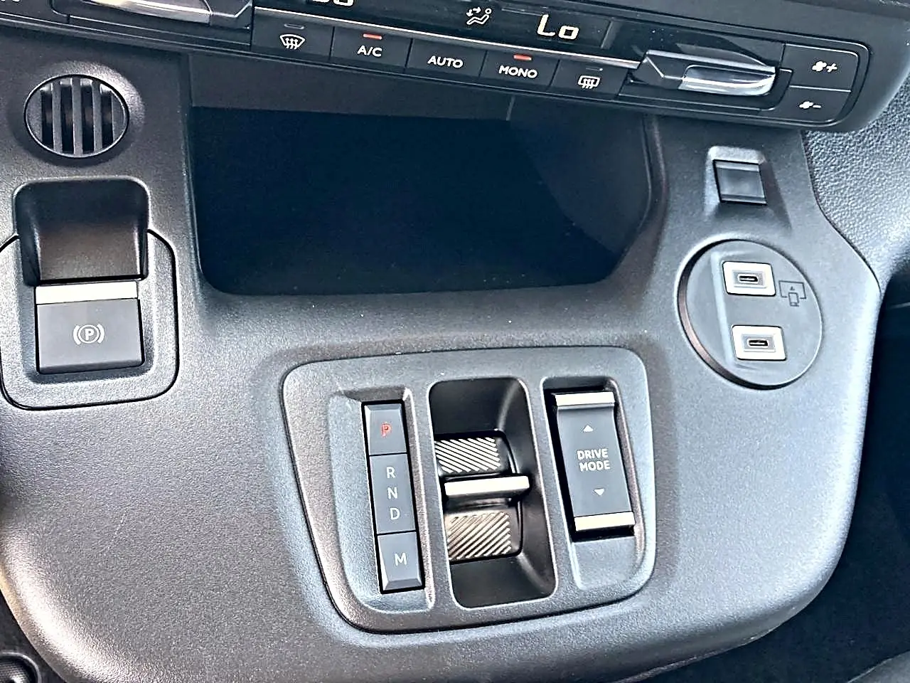 Gros plan sur la console centrale noire du Citroën Berlingo 2026 avec commandes de boîte auto et prises USB.