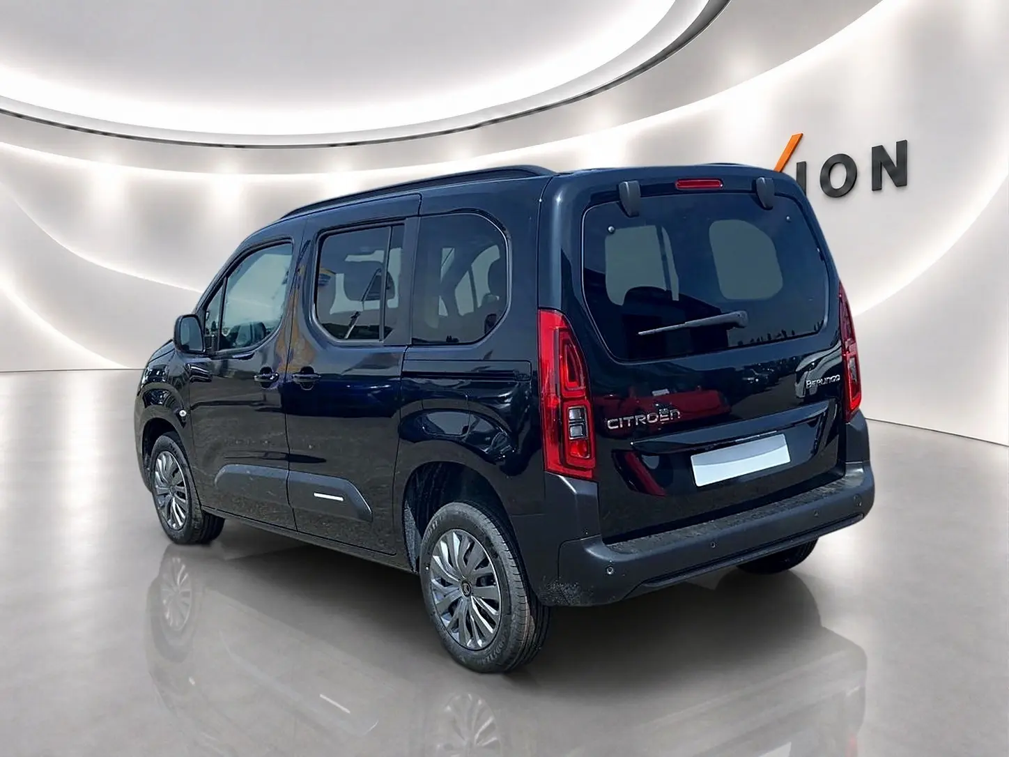Vue 3/4 arrière droite d’un Citroën Berlingo noir avec barres de toit et vitres arrière teintées dans un showroom.