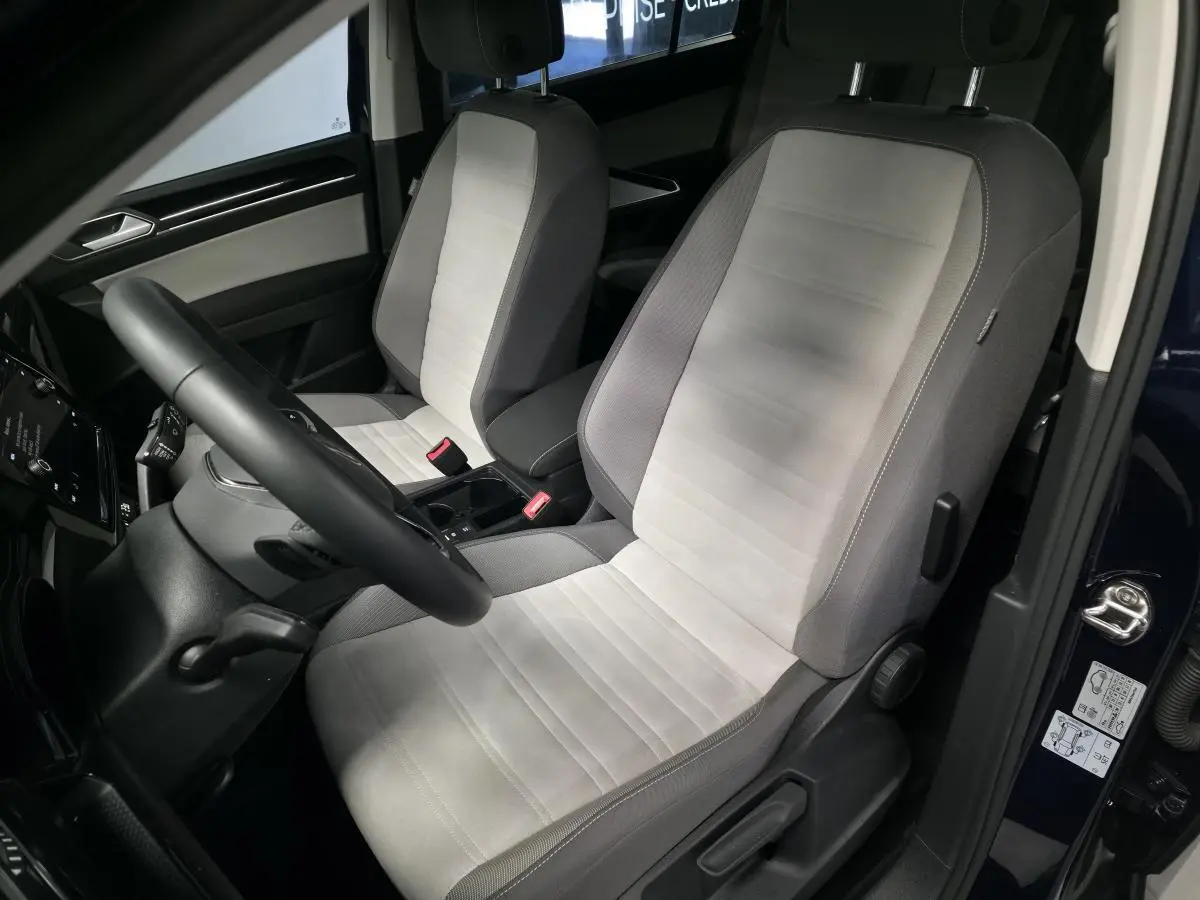 Intérieur côté conducteur du Volkswagen Touran bleu 2024, sièges en tissu gris clair et volant multifonction noir.
