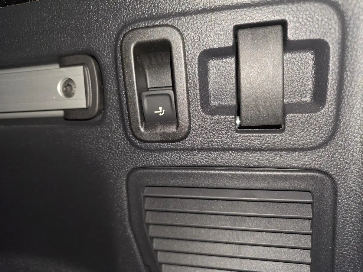 Gros plan sur le bouton de rabattement électrique des sièges dans le coffre du Volkswagen Touran bleu 2024.