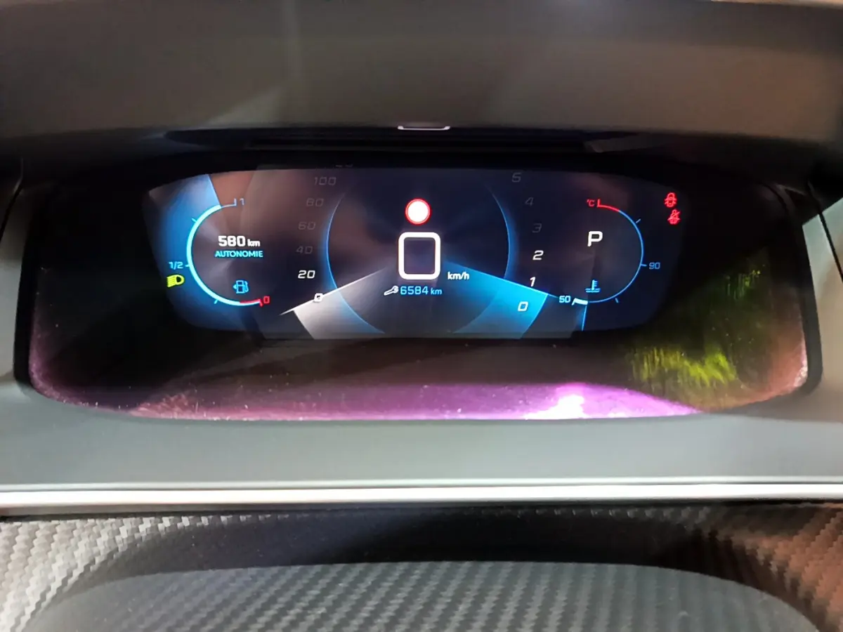 Affichage numérique du tableau de bord de la Peugeot 208 gris foncé, montrant vitesse, autonomie et indicateurs.