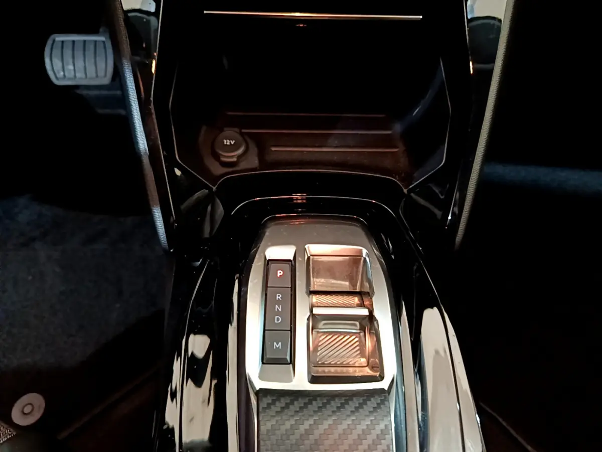 Gros plan sur la console centrale noire brillante avec levier de boîte automatique et bouton parking du Peugeot 208 gris foncé.
