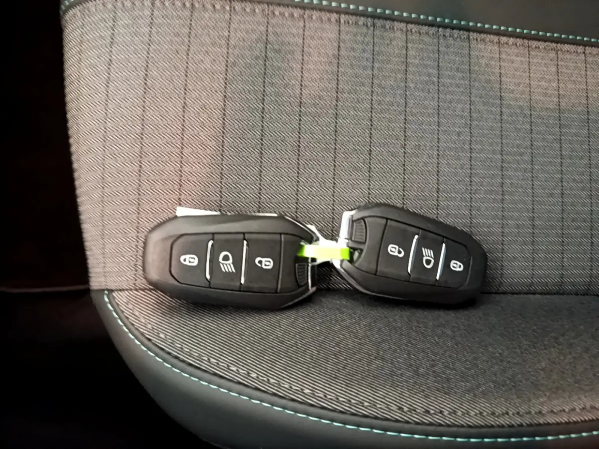 Deux clés de voiture Peugeot 208 posées sur un siège tissu gris foncé avec surpiqûres bleues, vue rapprochée intérieure.