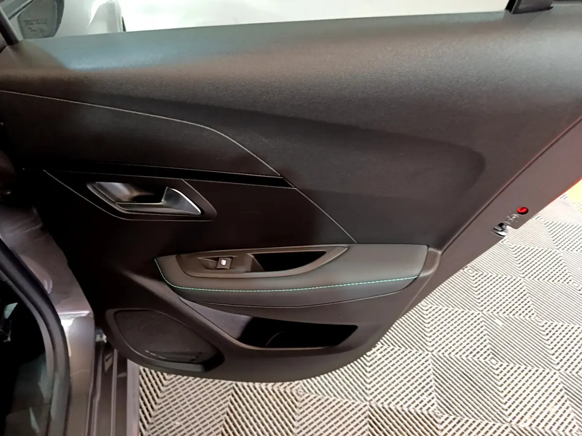 Vue intérieure du panneau de porte avant gauche de la Peugeot 208 gris foncé avec surpiqûres vertes et commande de vitre.