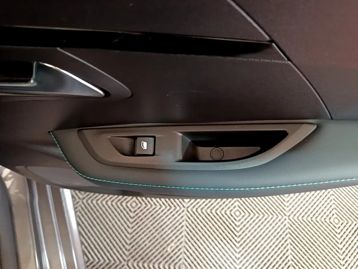 Poignée intérieure côté gauche de la porte d'une Peugeot 208 gris foncé avec couture bleue et bouton de verrouillage.