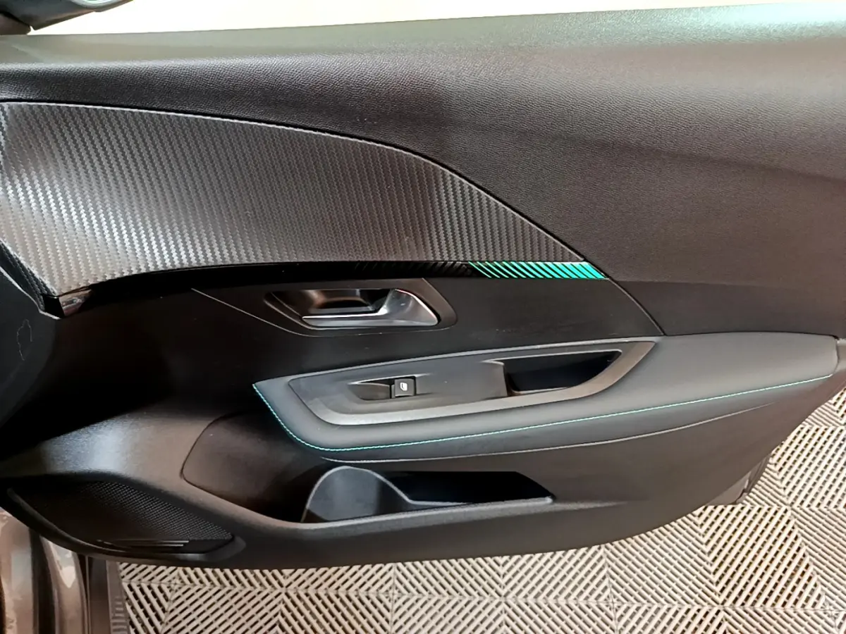 Gros plan sur la porte côté gauche de la Peugeot 208 gris foncé avec surpiqûres bleues et insert décoratif texturé.
