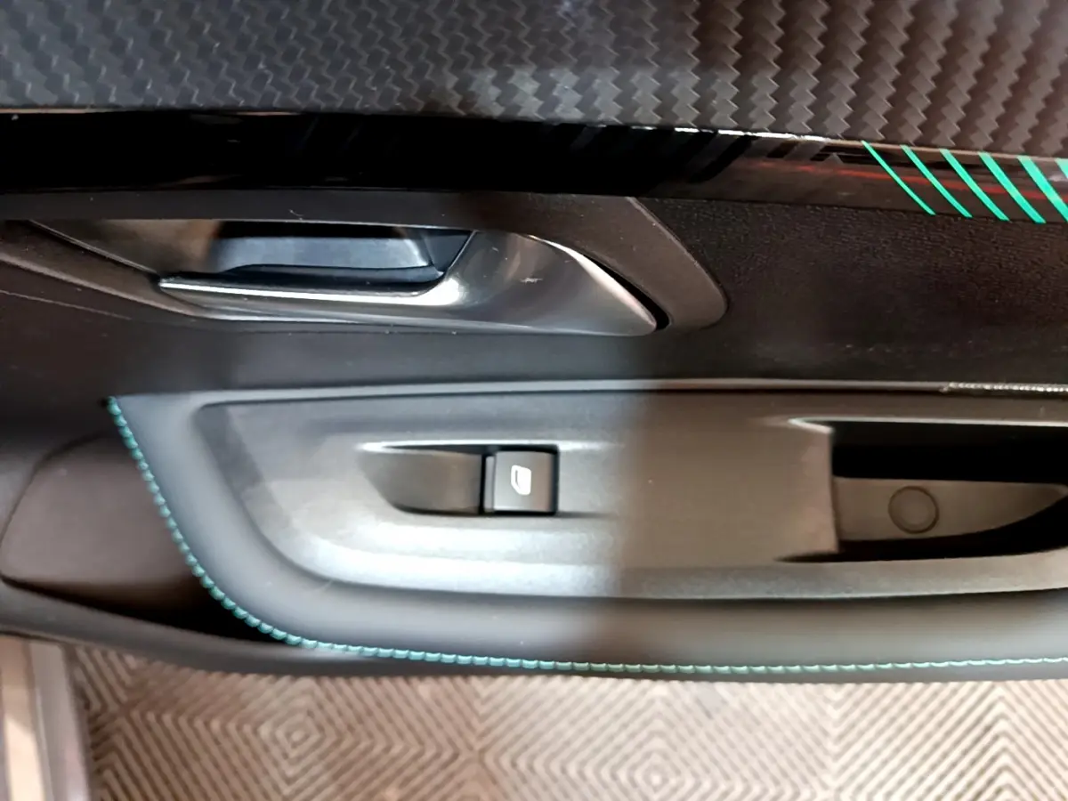 Gros plan sur la poignée intérieure côté gauche de la porte d'une Peugeot 208 gris foncé avec surpiqûres bleues.