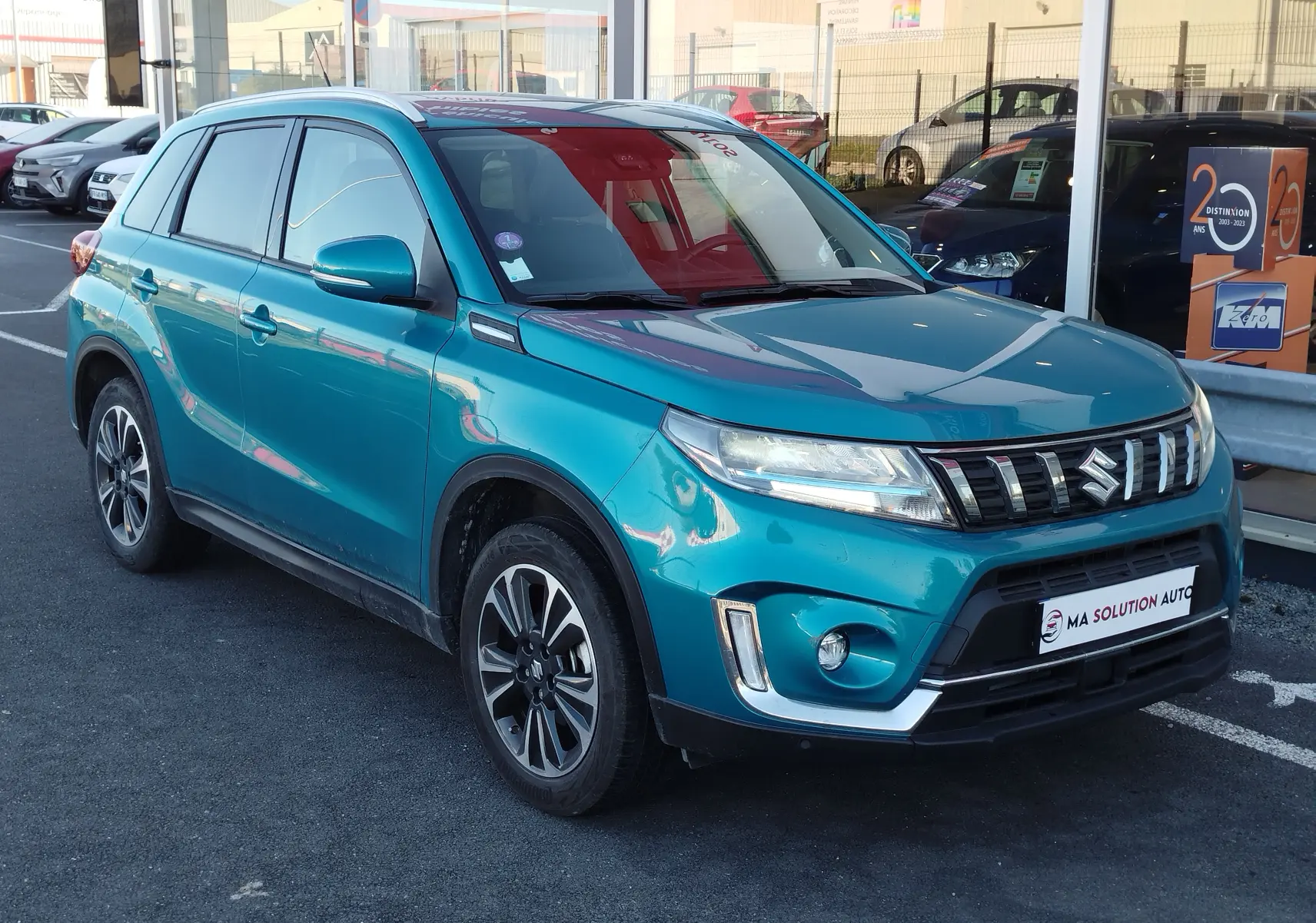 Suzuki Vitara 2023 turquoise en 3/4 avant droit, avec calandre chromée et jantes alliage bicolores.