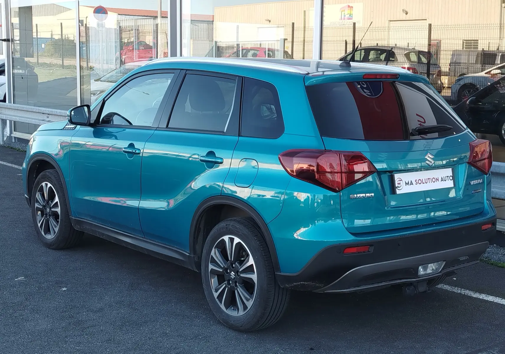 Vue 3/4 arrière droite d'un Suzuki Vitara 2023 turquoise métallisé avec jantes alliage et vitres teintées.