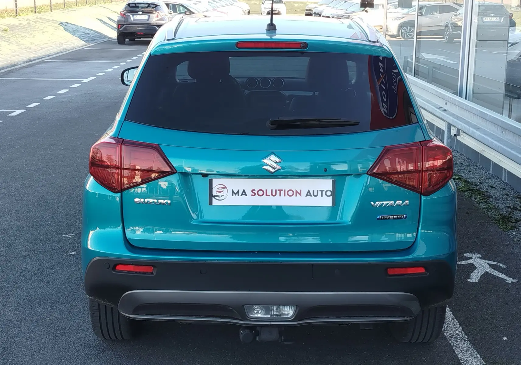 Vue arrière d'un Suzuki Vitara 2023 hybride en turquoise métallisé, avec logo et feux arrière distinctifs visibles.
