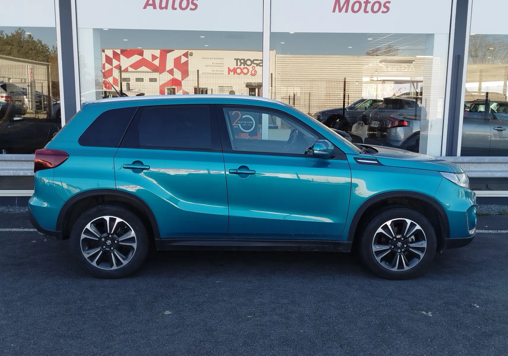 Profil droit d'un Suzuki Vitara 2023 en bleu turquoise métallisé, avec jantes alliage bicolores et vitres teintées.