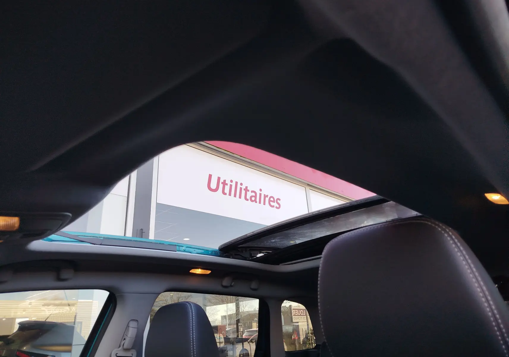 Vue intérieure du toit ouvrant panoramique du Suzuki Vitara turquoise, avec sièges avant en cuir noir et lumière d'ambiance allumée.