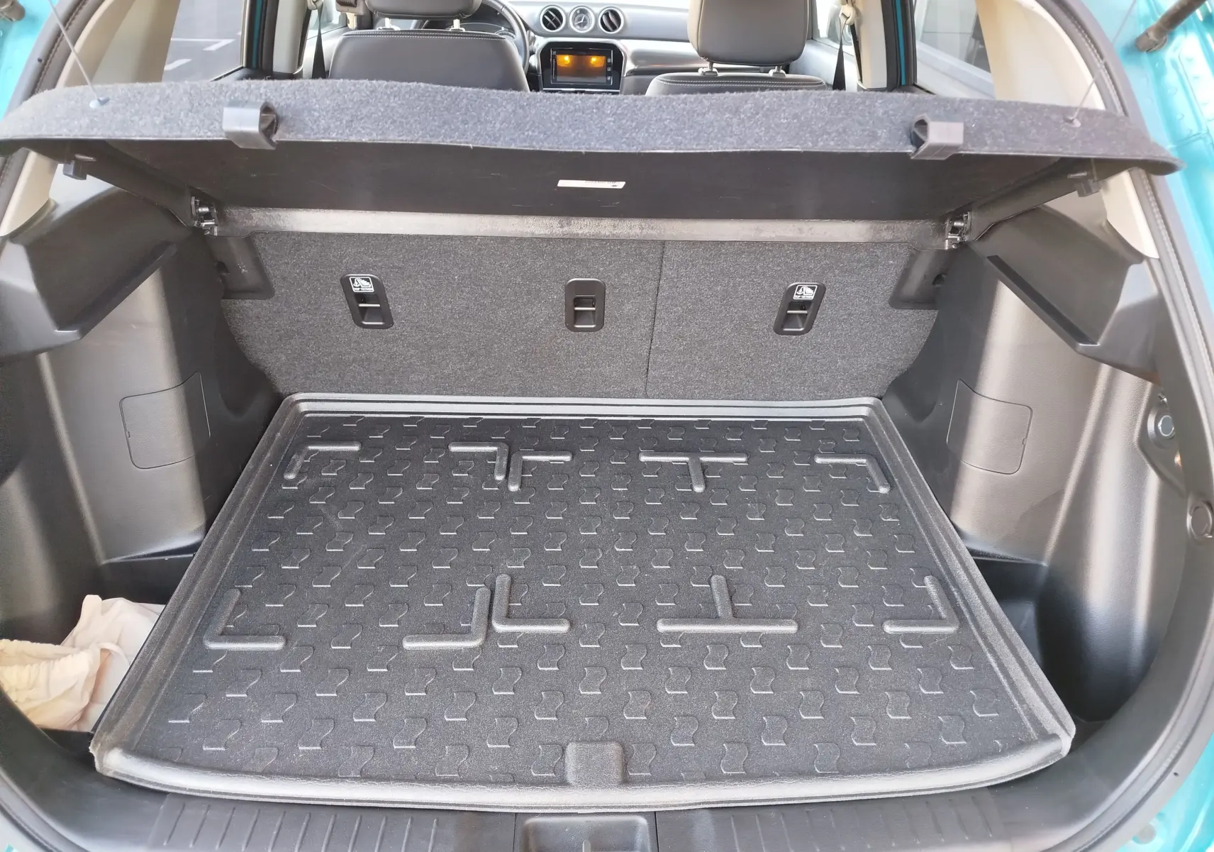 Vue arrière du coffre ouvert du Suzuki Vitara 2023 en turquoise Atlantis, avec tapis de protection noir et intérieur gris.