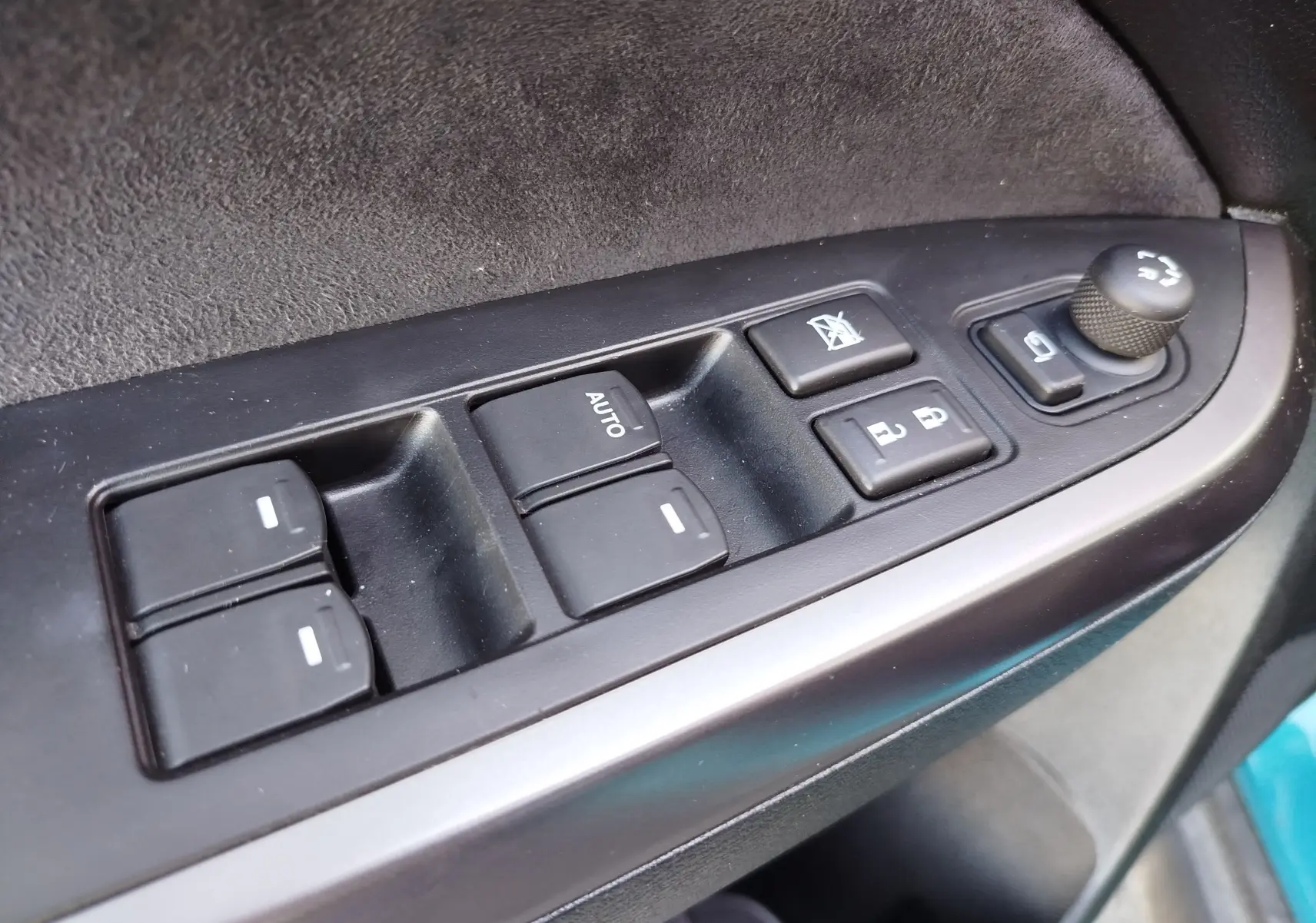 Gros plan sur les commandes des vitres et rétroviseurs côté conducteur d’un Suzuki Vitara turquoise 2023.