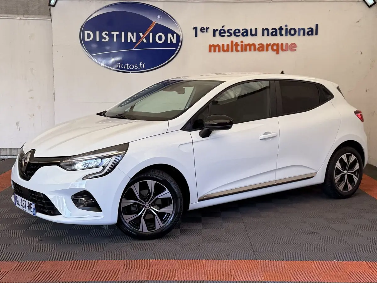 Renault Clio Business blanc vue 3/4 avant droit, jantes noires et logo Distinxion en arrière-plan.