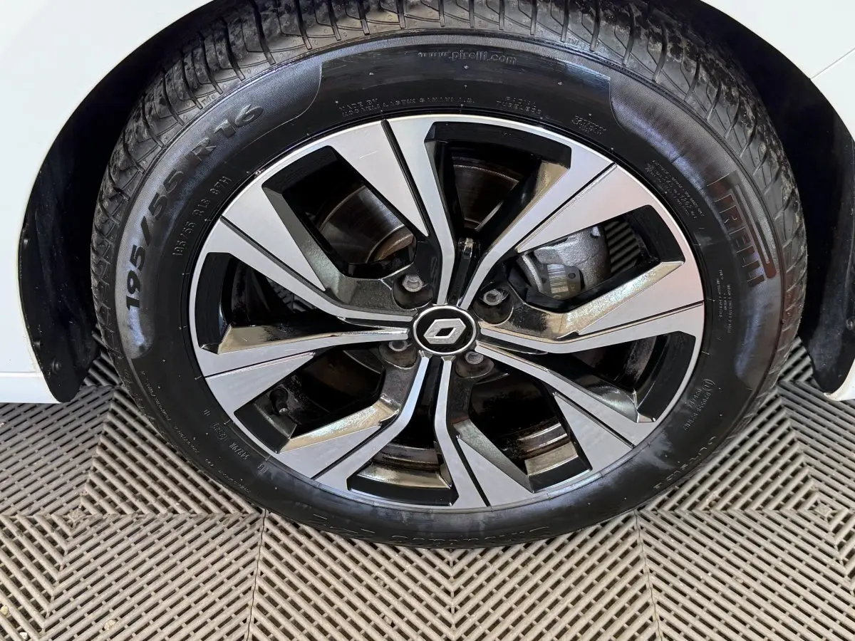 Gros plan sur la roue avant droite d'une Renault Clio blanche avec jante alliage bicolore et logo central Renault.