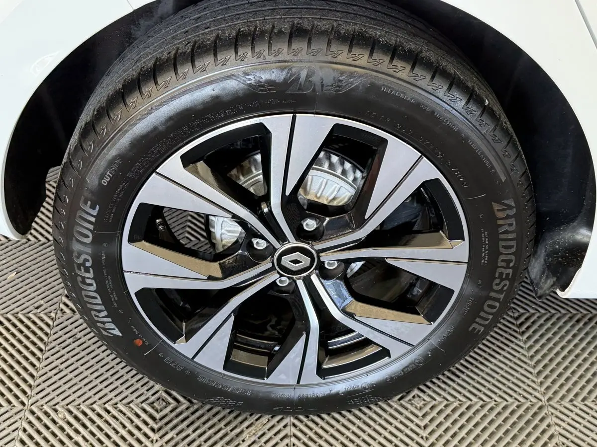 Gros plan sur la roue avant droite d'une Renault Clio blanche 2023 avec jante alliage bicolore et pneu Bridgestone.