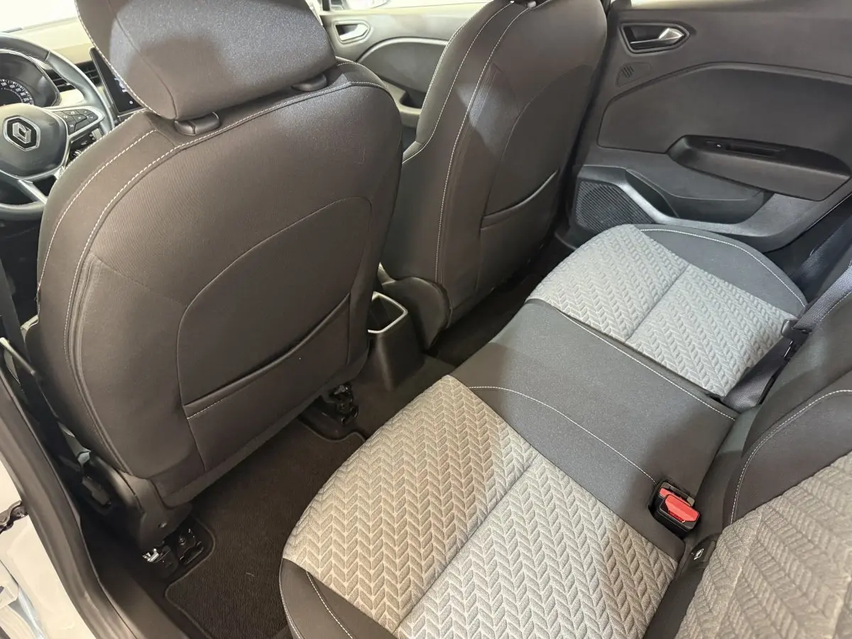 Vue intérieure arrière côté droit de la Renault Clio blanche 2023, montrant les sièges tissu bicolores et le tableau de bord partiel.