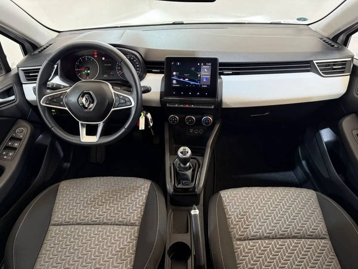 Vue intérieure avant de la Renault Clio Business 2023, tableau de bord noir et blanc avec écran tactile central et volant multifonctions.
