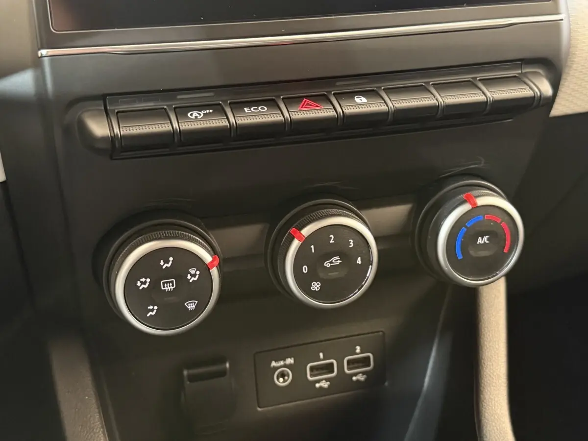 Gros plan sur les commandes de climatisation et les ports USB du tableau de bord noir de la Renault Clio blanche.