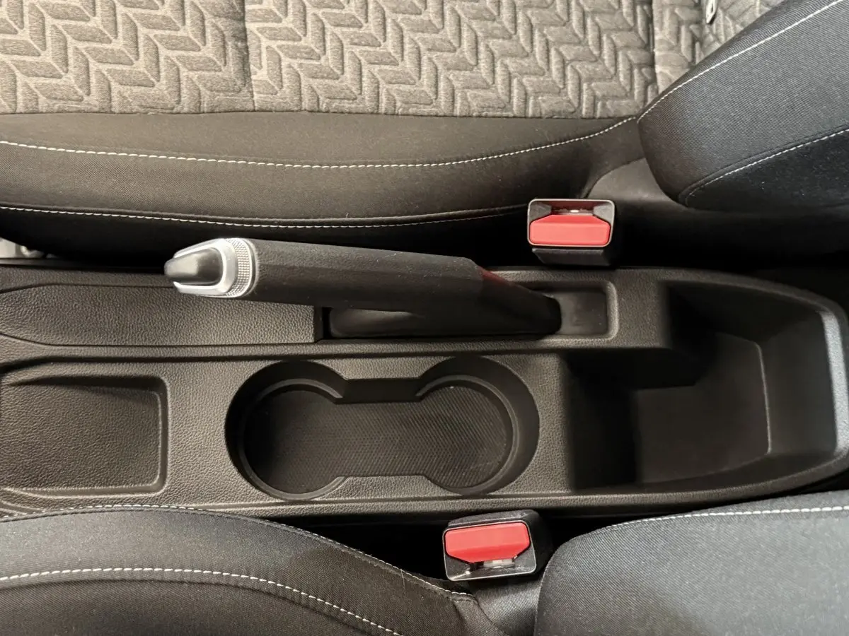 Vue plongeante sur le frein à main manuel et porte-gobelets entre les sièges noirs de la Renault Clio Business blanche.