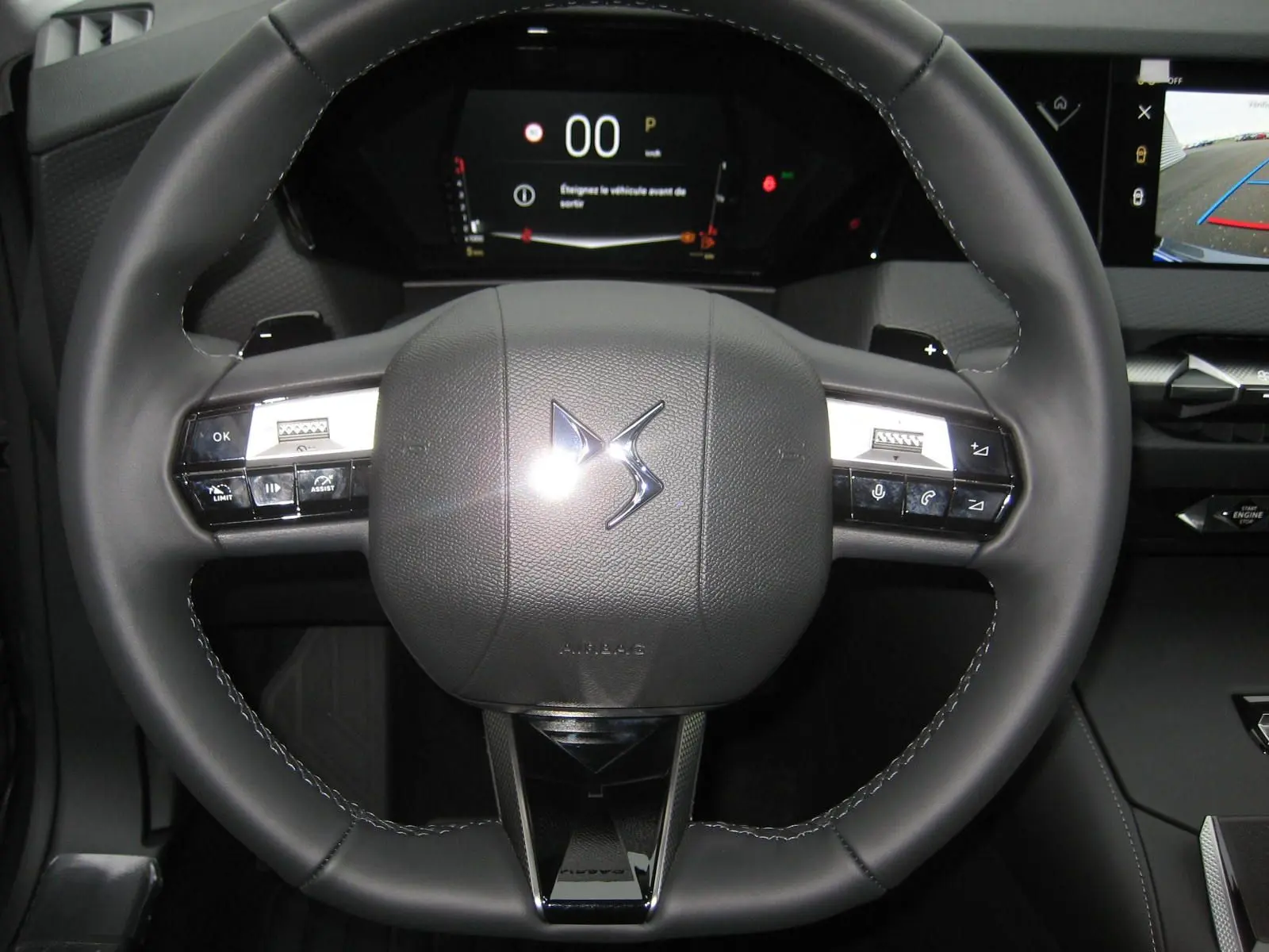 Gros plan sur le volant en cuir noir du DS4 2024 avec commandes intégrées et tableau de bord numérique en arrière-plan.