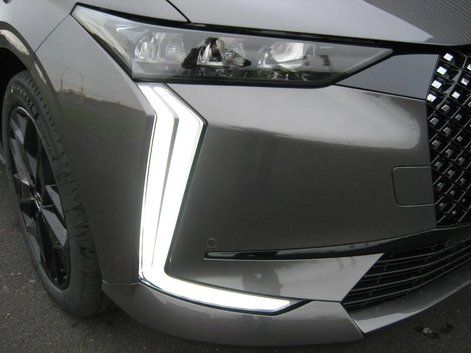 Gros plan sur le phare avant gauche et la signature lumineuse en forme de flèche du DS4 gris platinium 2024.