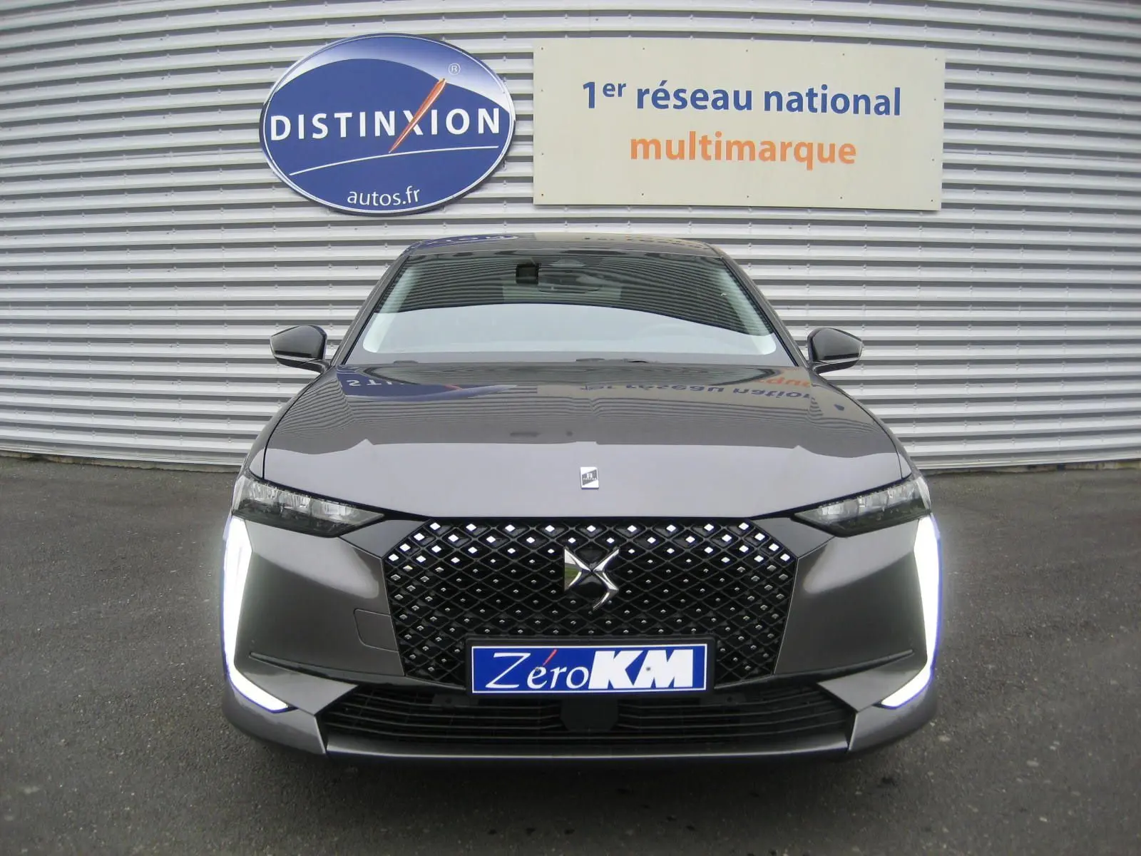Vue frontale d'une DS4 2024 gris platinium avec calandre noire à motif losange et feux LED verticaux allumés.