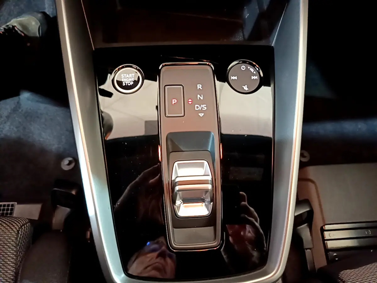 Vue plongeante sur la console centrale noire brillante de l'Audi A3 35 TFSI avec levier de vitesses automatique et bouton start-stop.