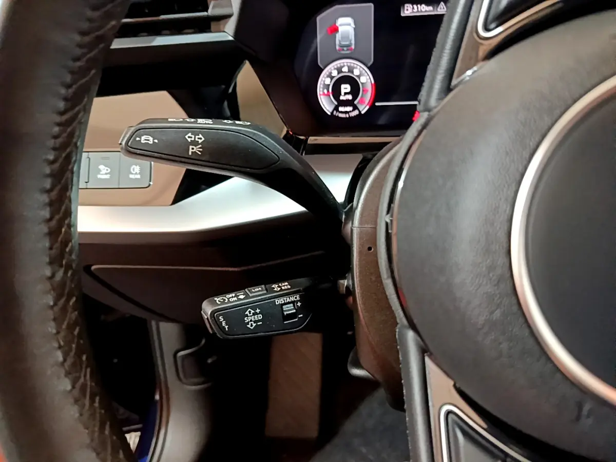 Gros plan sur le volant noir et les commandes au volant côté gauche de l'Audi A3 35 TFSI 2023 avec affichage numérique.