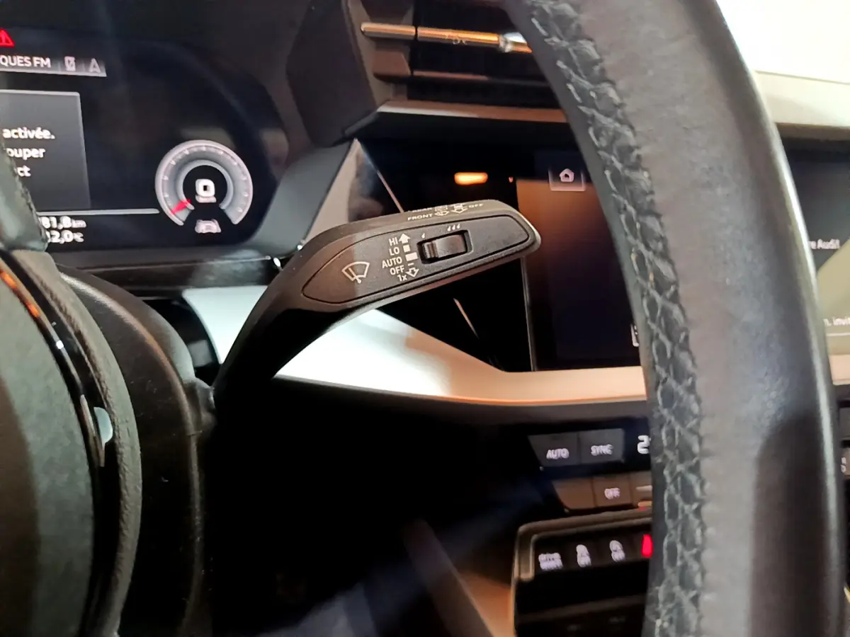 Gros plan sur le commodo d’essuie-glace à gauche du volant cuir dans l’habitacle de l’Audi A3 bleu 2023.