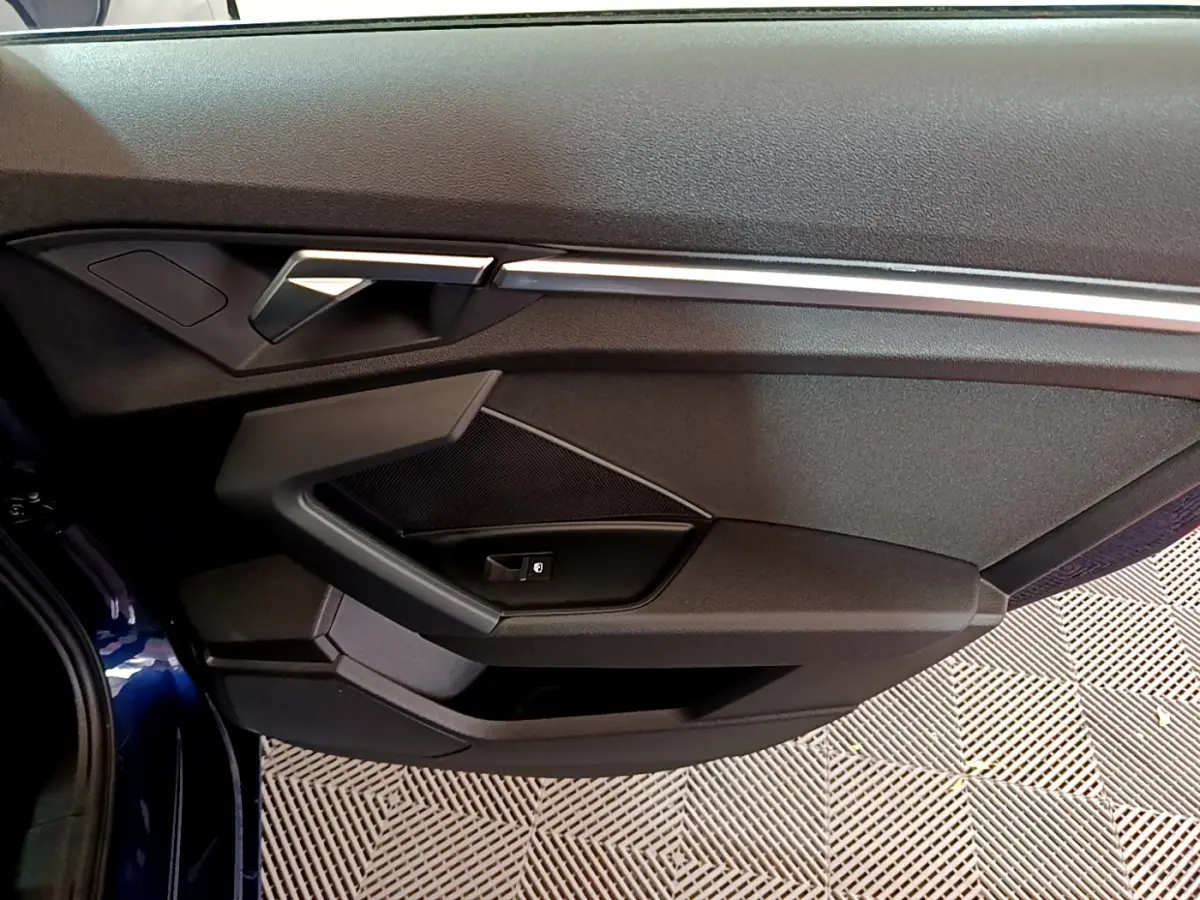 Vue rapprochée de la porte côté gauche de l'Audi A3 bleu 2023, avec poignée et commandes intégrées.