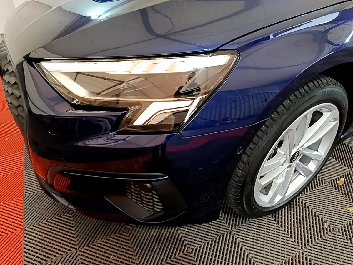 Gros plan sur l'avant droit bleu d'une Audi A3 35 TFSI 150 MHEV avec phare LED et jante argentée.
